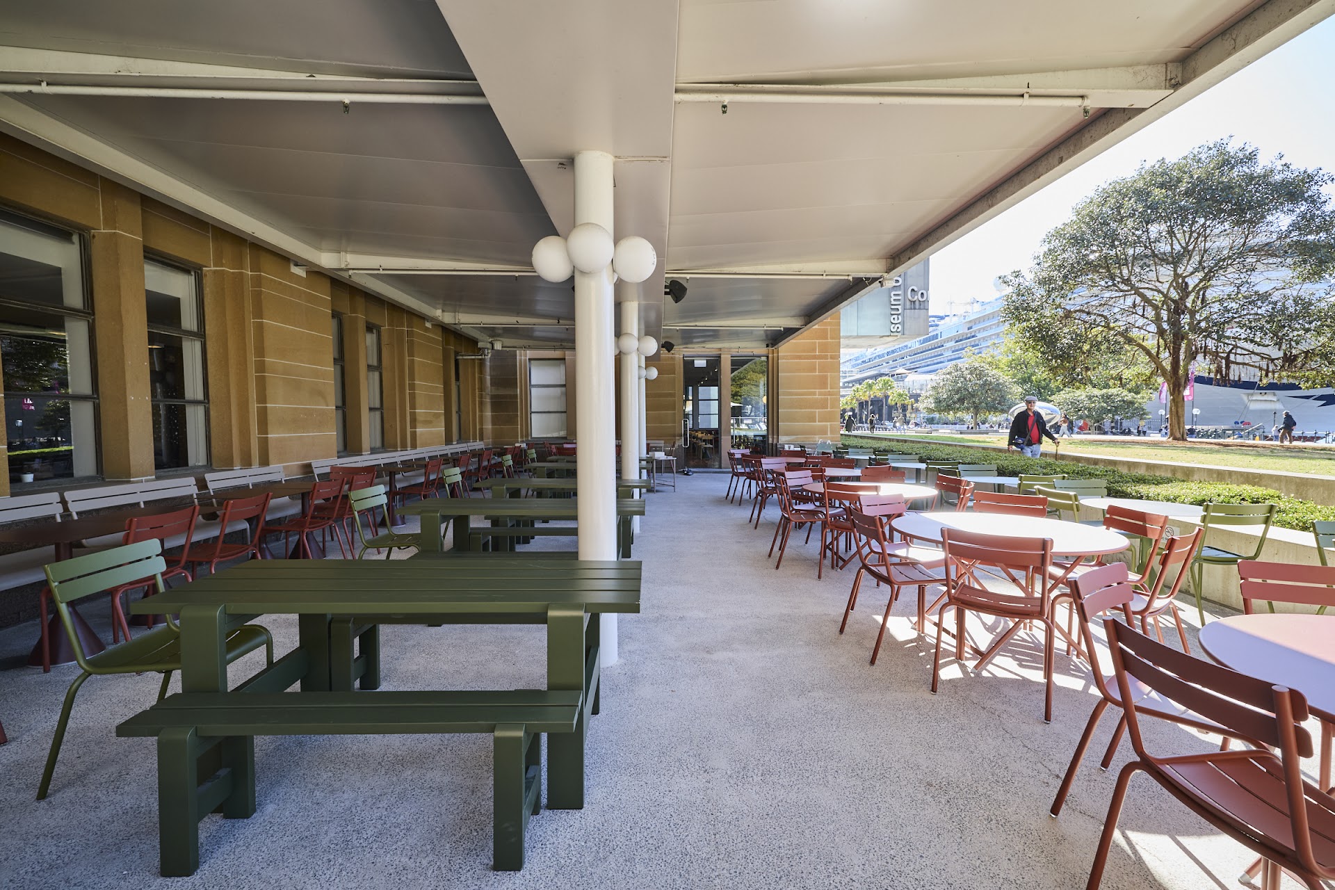 Covered MCA Cafe terrace with red and green outdoor tables near Sydney Harbour